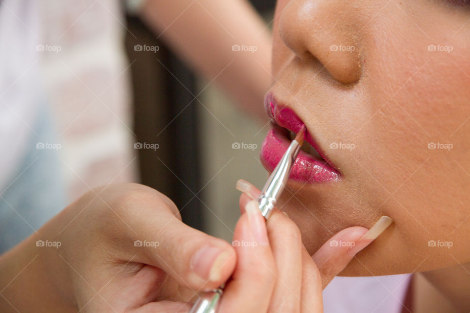 Close-up of beautician applying lipstick to bride