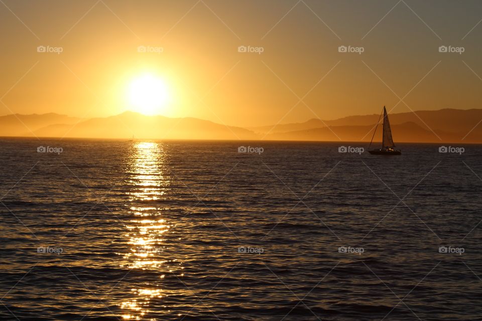 golden hour, sunset cross the waters over the mountains as a sailboat sails by