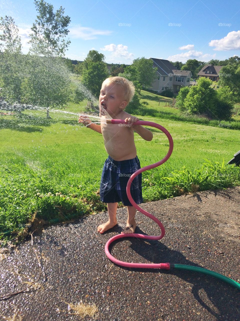 Little cute child boy playing with a rubber hose in the garden