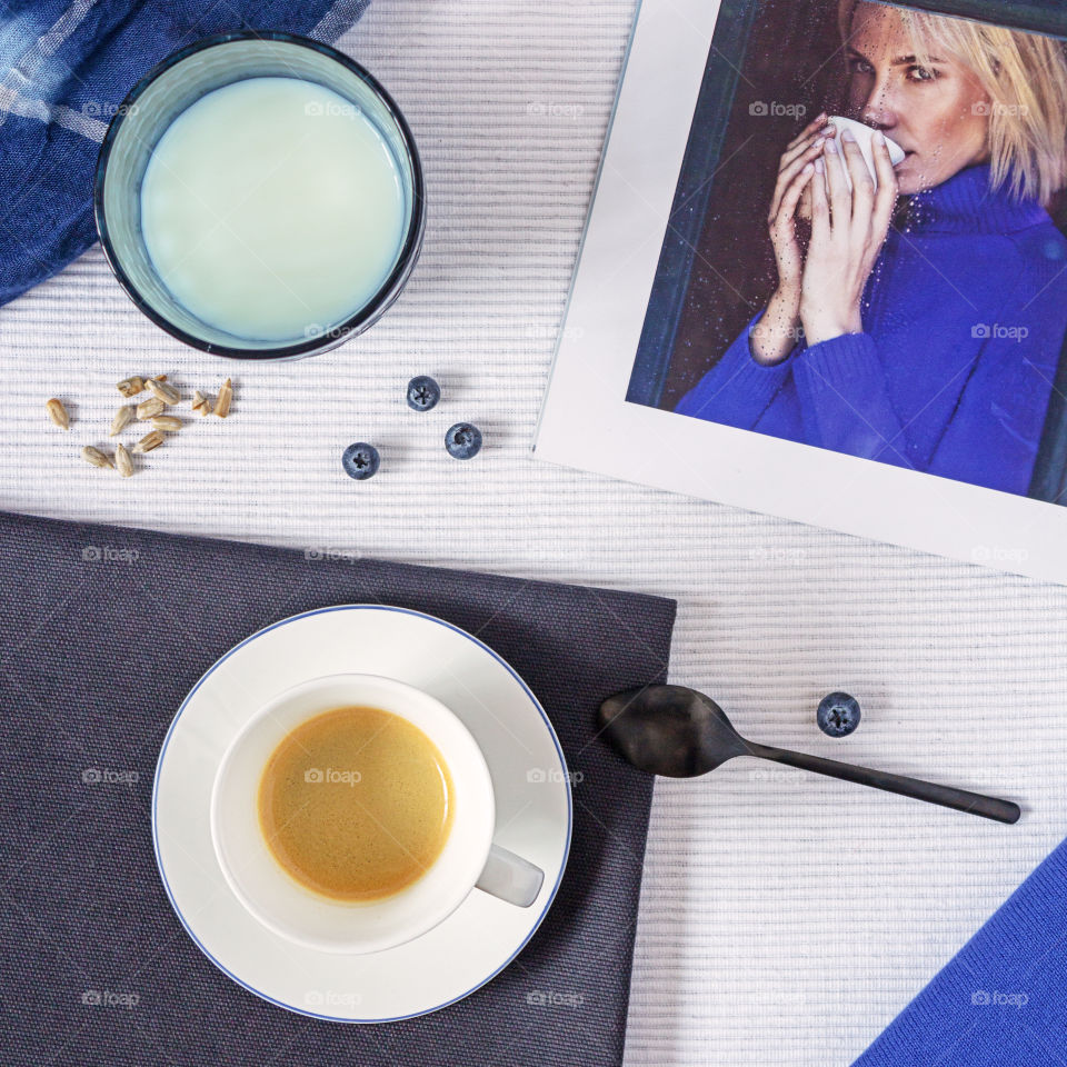Morning coffee with a fashion magazine.  Food photo, square orientation, flat lay.  Girl's breakfast: a cup of coffee on a linen textile napkin with a magazine, with blueberries, seeds and a glass of milk.  Healthy breakfast