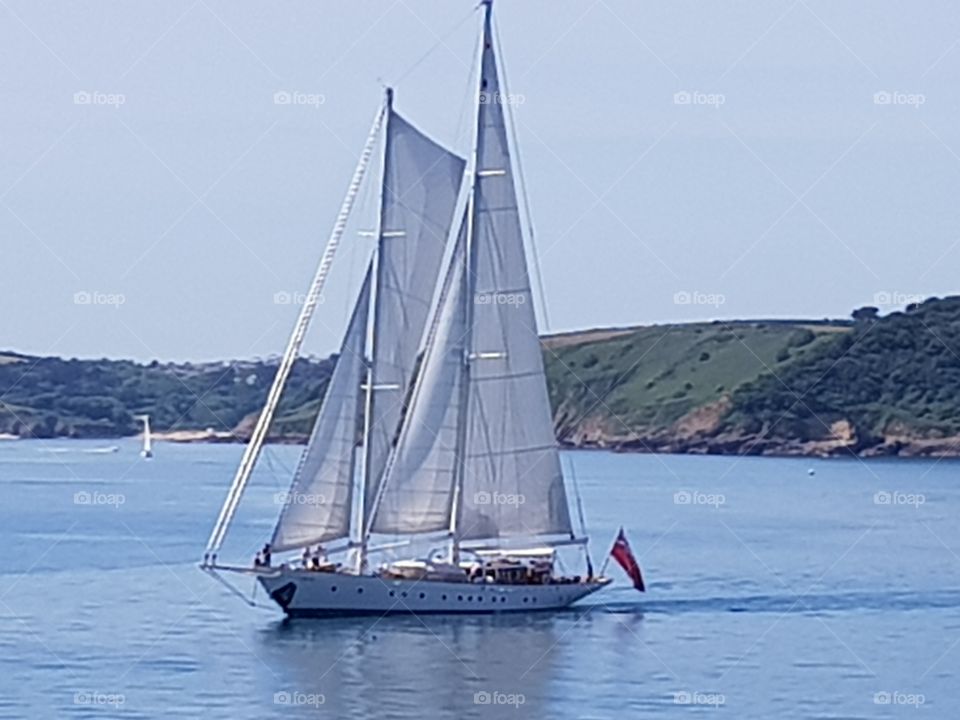 yacht sailing a calm sea on a beautiful sunny day with a coastal backdrop