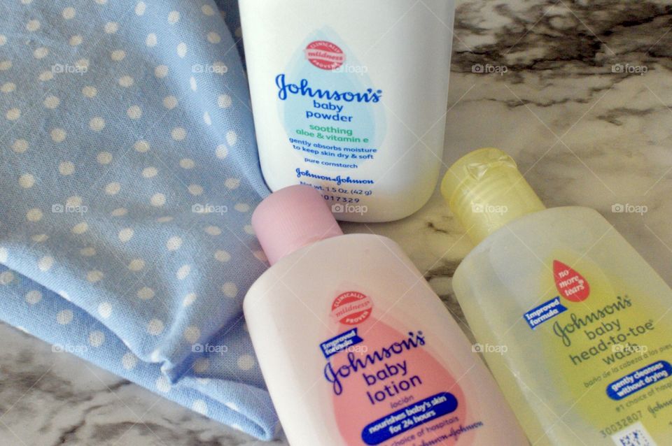 Johnson and Johnson baby powder, lotion, and head to toe body wash on a white marble background with a blue and white polkadot linen