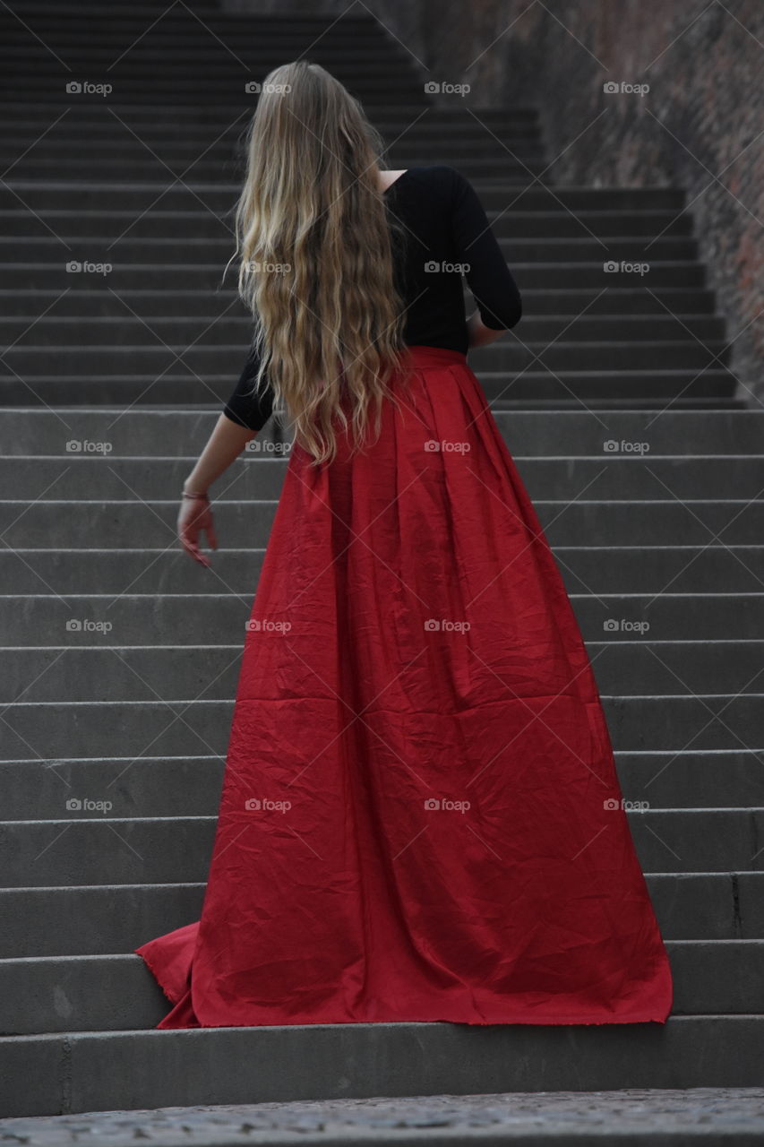 Blonde long hair woman in long red skirt standing on the stairs in old Prague