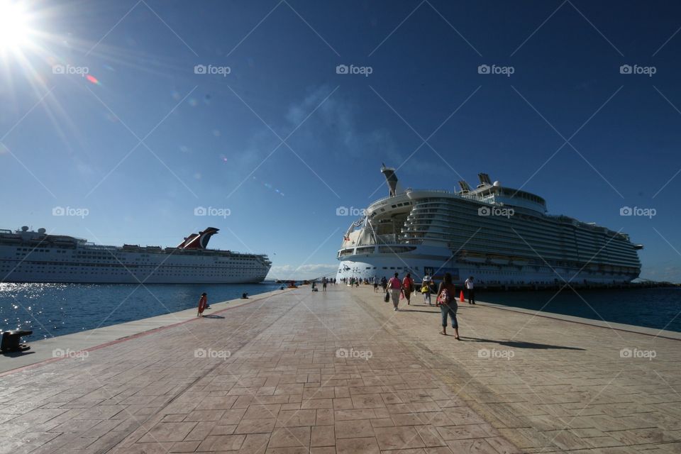 View of the deck leading up to a cruise ship in a sunny, tropical port. 