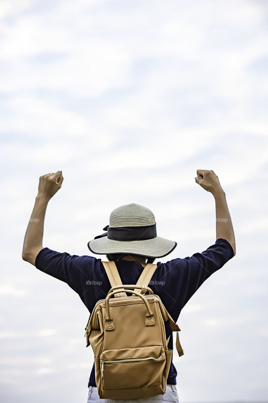 Women shoulder backpack and  raise their arms up to the sky.