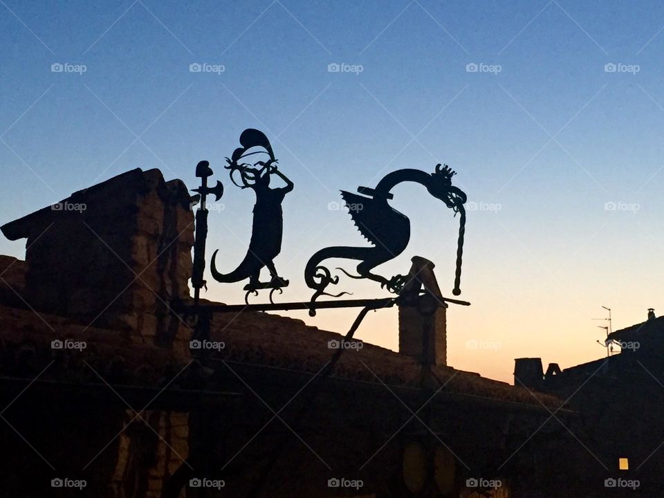 Wind vane silhouettes representing mythological figures, on  one of the roofs of Assisi, medieval Italian village, at sunset 