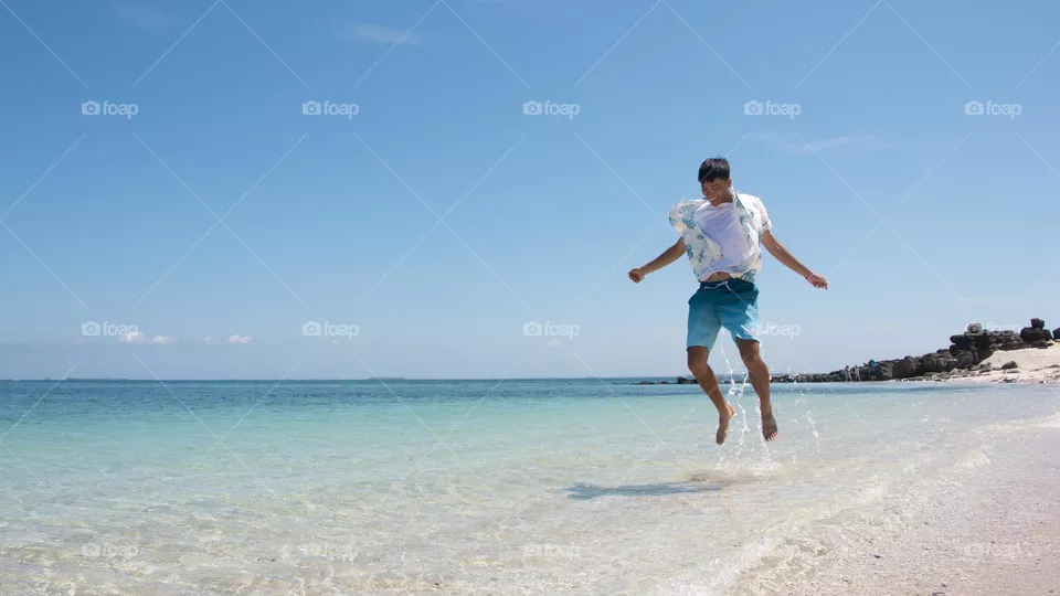 Holidays and people-A happy young man wearing swimwear  jumping on the beach with copy space. Summer travel adventure vacation at tropical beach on Jibei Islanda, Penghu County, Taiwan.