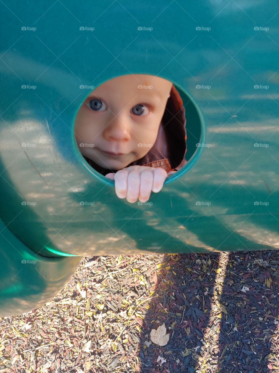toddler peaking out window in tube at park