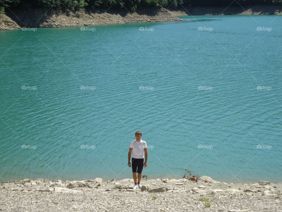 A man at the lake. A man is getting on the hill in front of at the blue lake