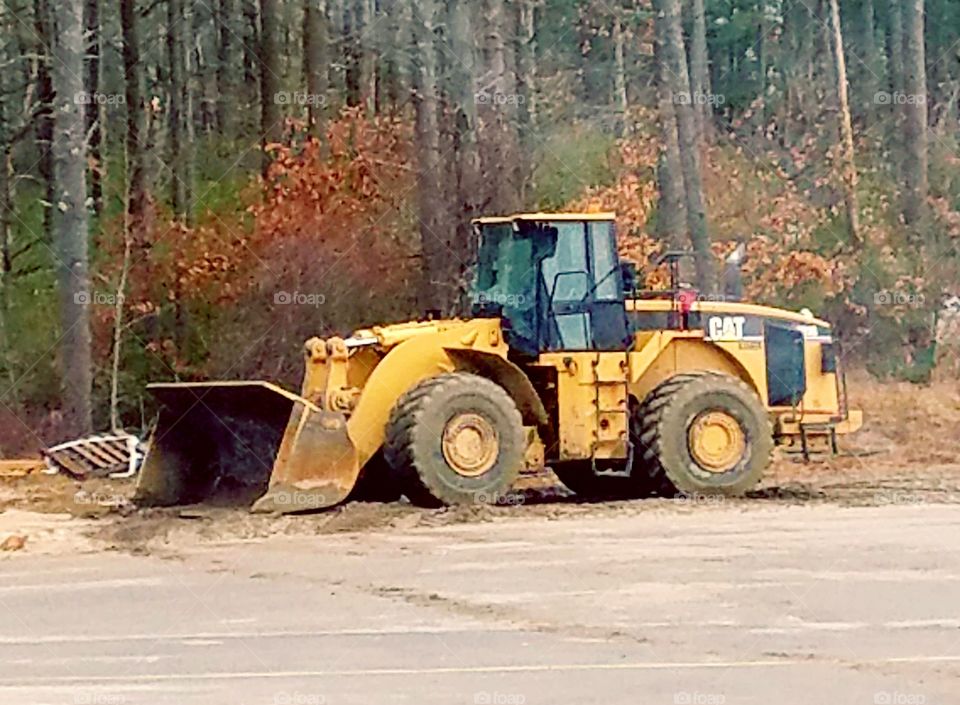Old tractor 🚜 parked in job site near treeline. Bulldozer bucket in down position.