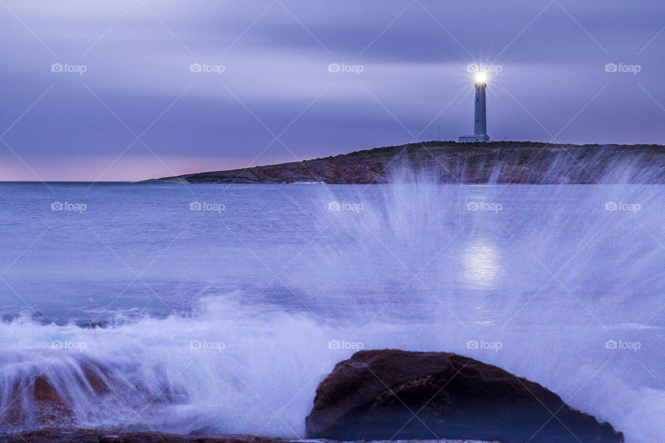 Cape Leeuwin lighthouse dwarfed by rocky outcrops and waves crashing and splashing over the rocks in the bay at Augusta in South West Western