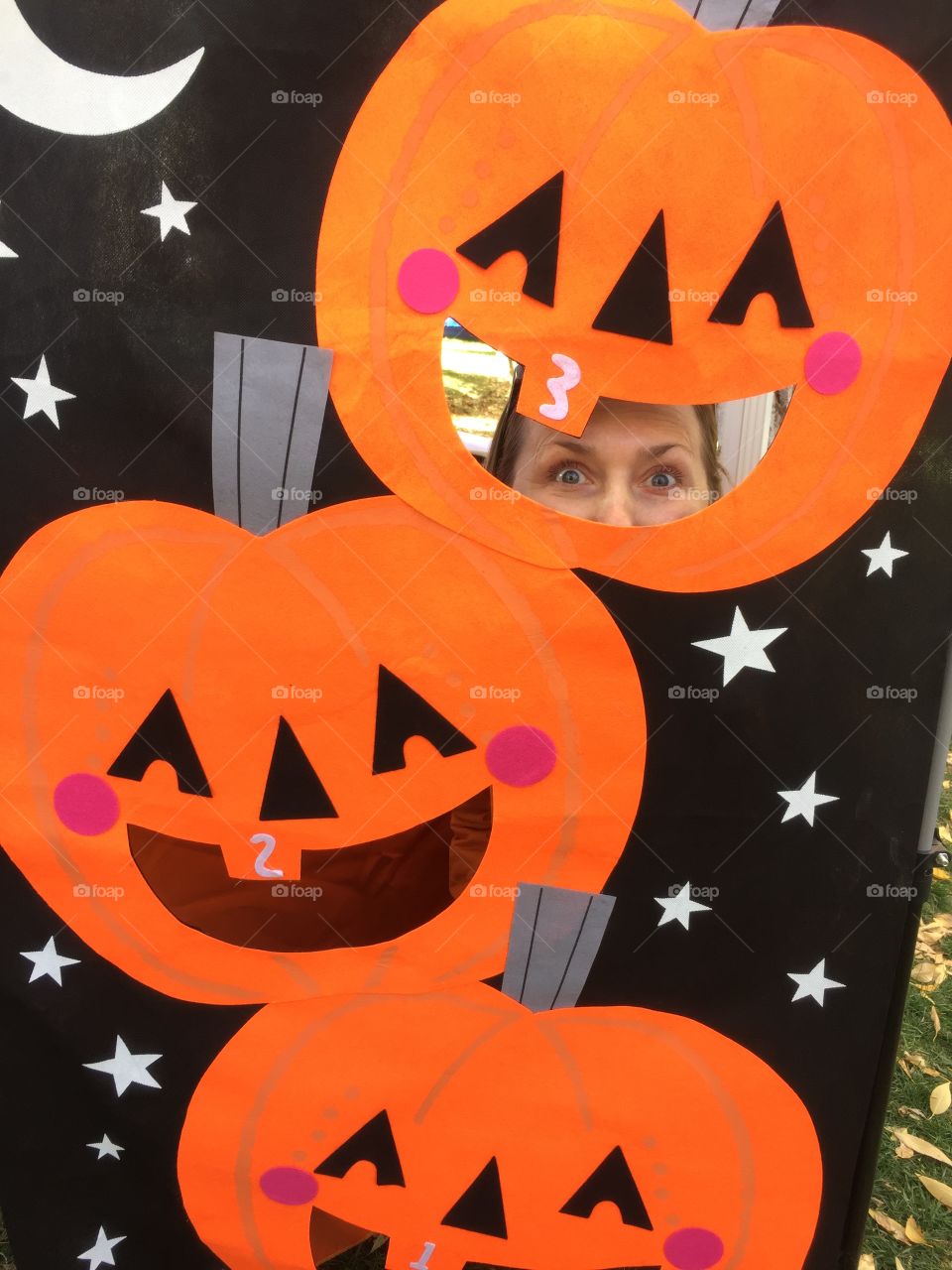 Girl hiding behind a stand with picture of carved pumpkins. Fall, pumpkins, fun.