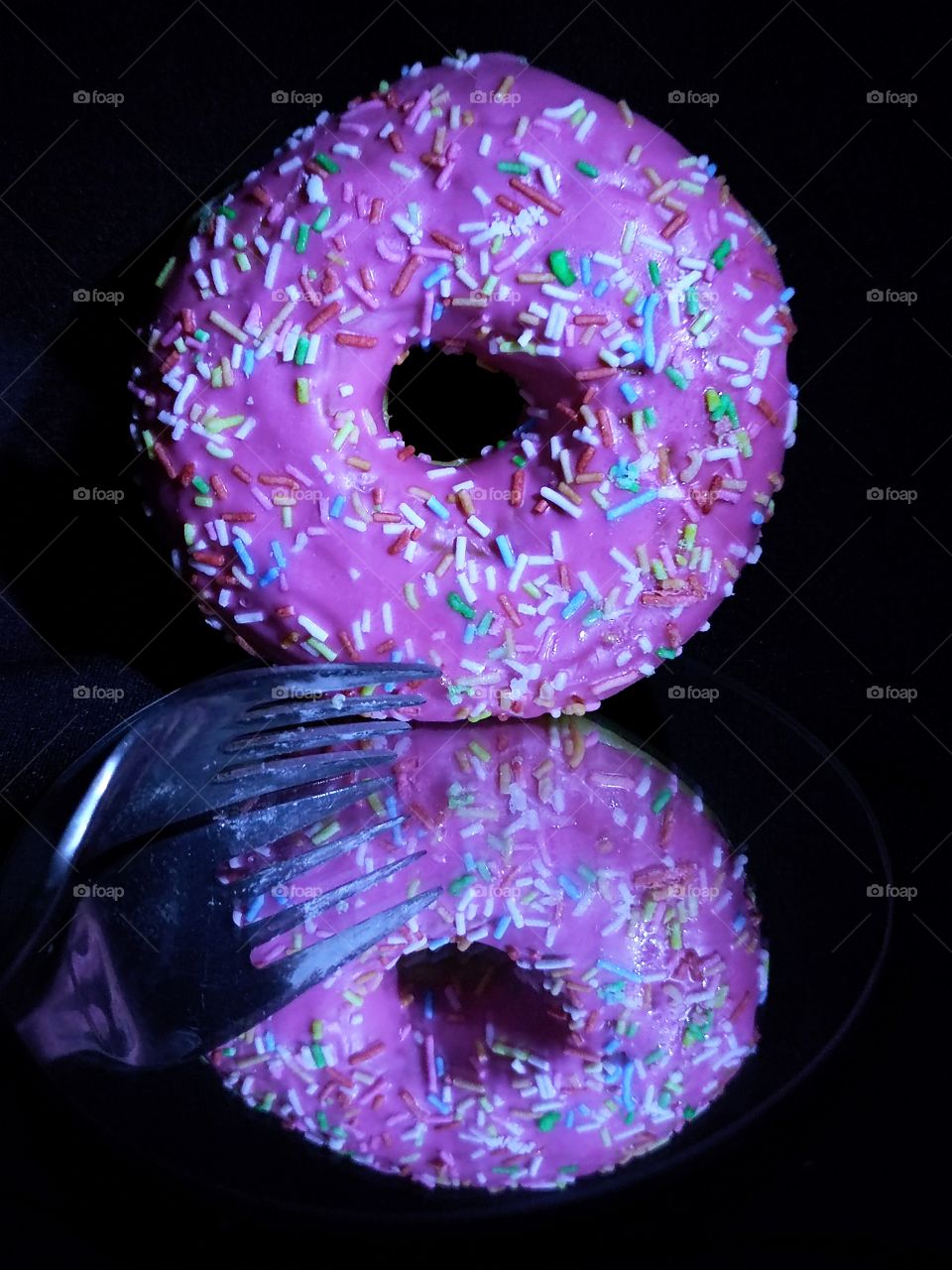 Reflection.  Multicolored donut and metal fork in the reflection of the mirror