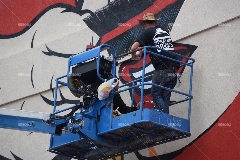 Artists painting large mural on building. 