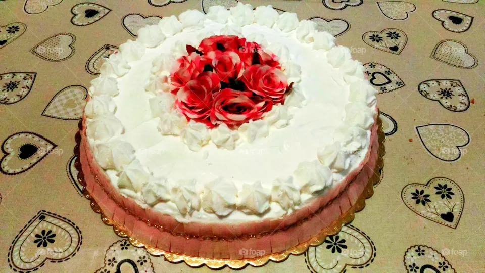 Homemade milk cream cake decorated with roses on a grey heart-patterned tablecloth
