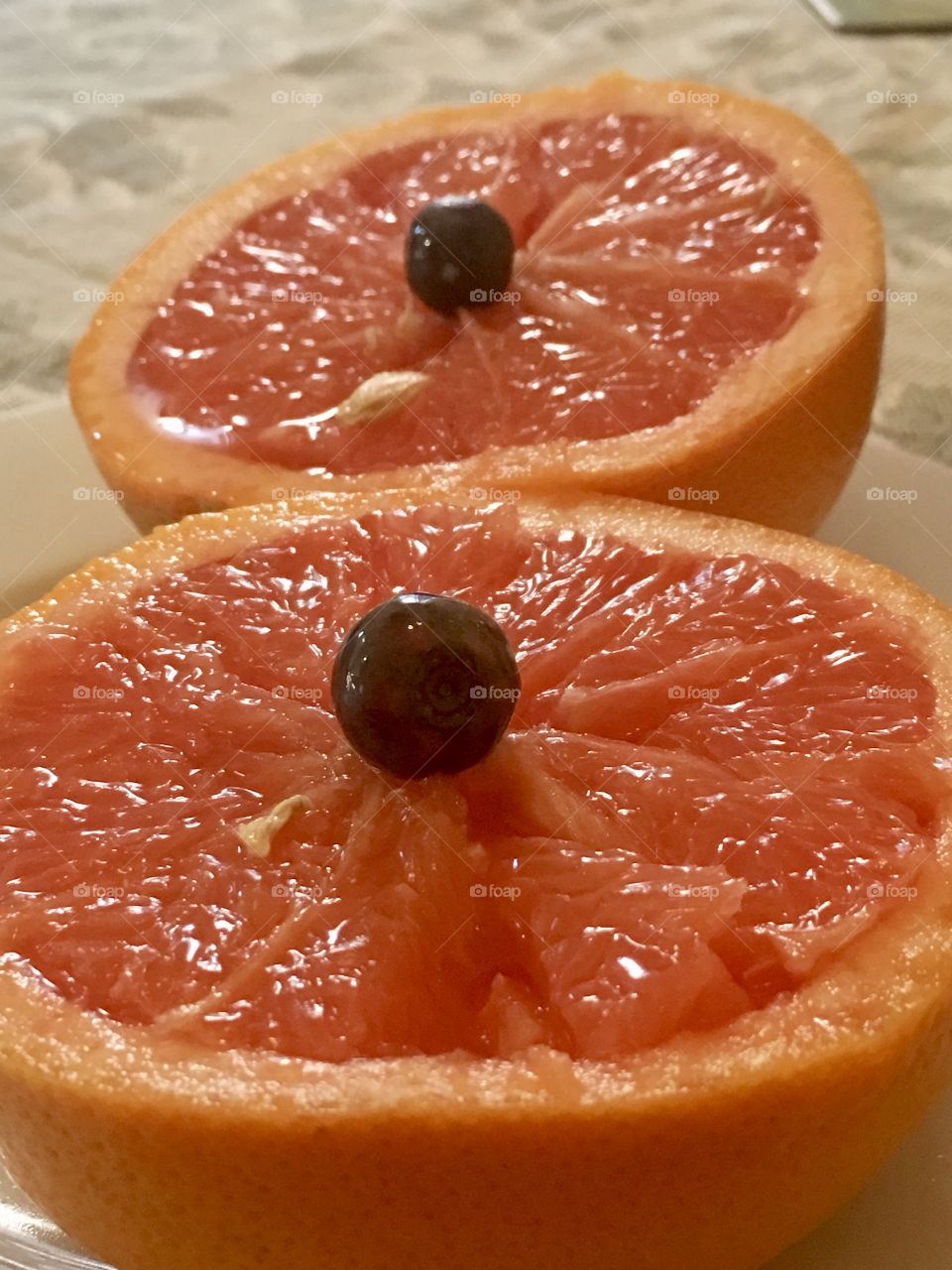 Juicy organic pink grapefruit, halved and prepared on white plate with blueberries in centre, closeup, citrus growers, healthy fruit and food, vitamins combat colds and flu