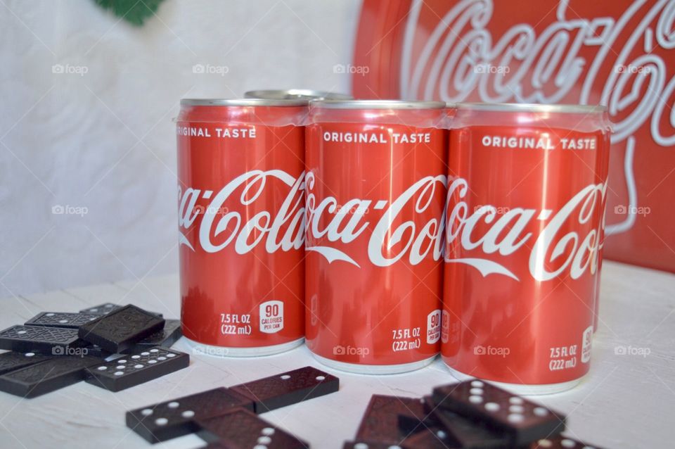 A six pack of Coca-Cola cans with dominoes