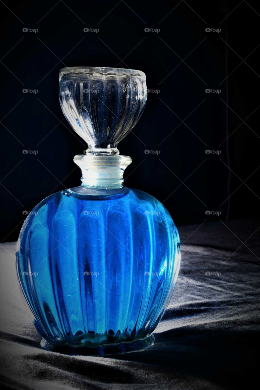 large clear glass pwrfume bottle with blue liquid low key picture