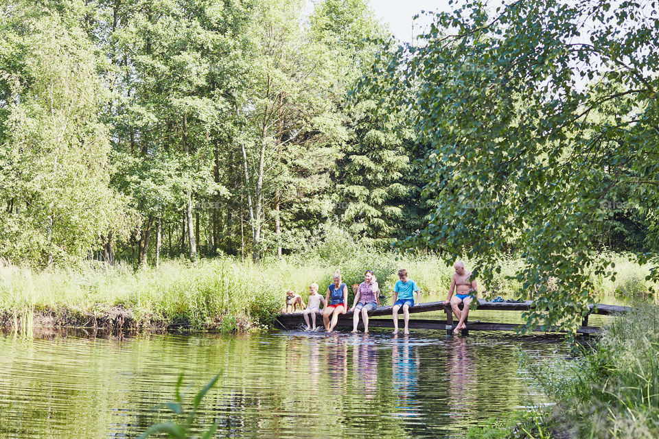 Family spending time together sitting on a bridge over a lake, among the trees, close to nature, during summer vacations. Candid people, real moments, authentic situations