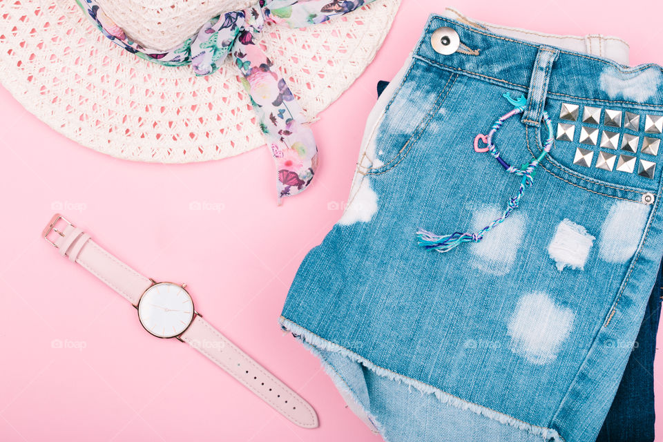 Female girly clothes, blue jeans shorts, hat, watch on pink background