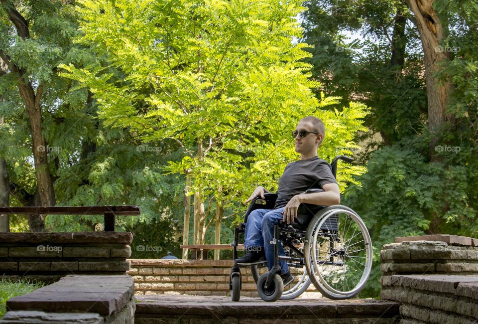 A blind man in a wheelchair rests in the park