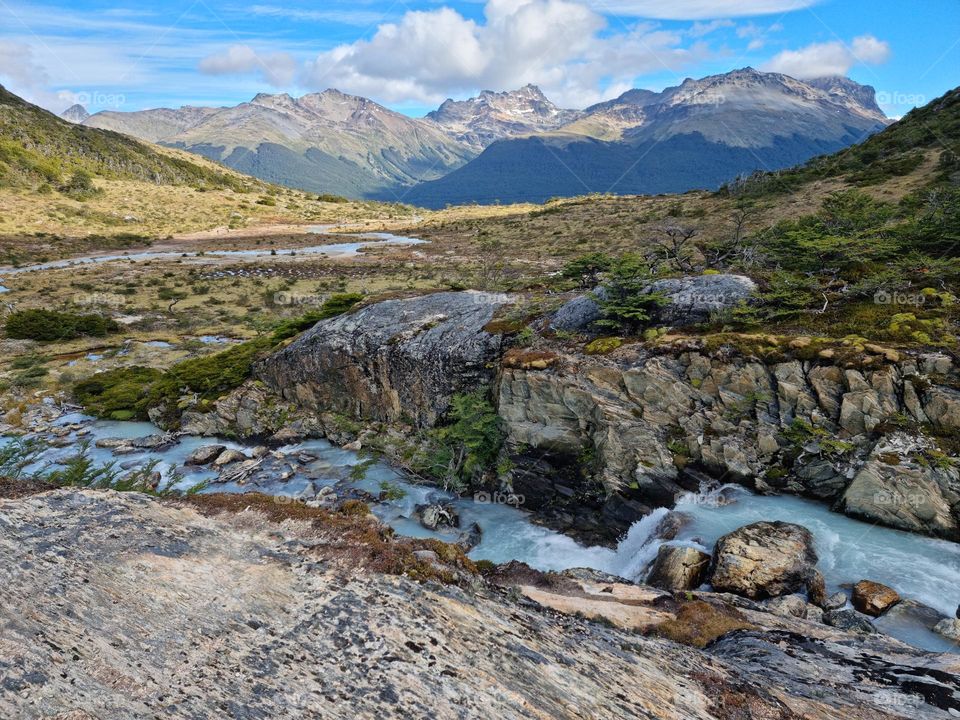 A river of turquoise water going through cliffs, green vegetation and mountains in the background.