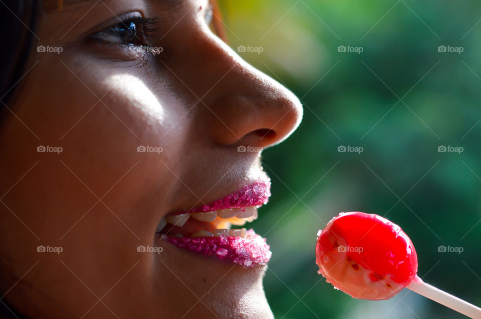 Beautiful woman with sugar coated pink lips, licking sugary lollipop.