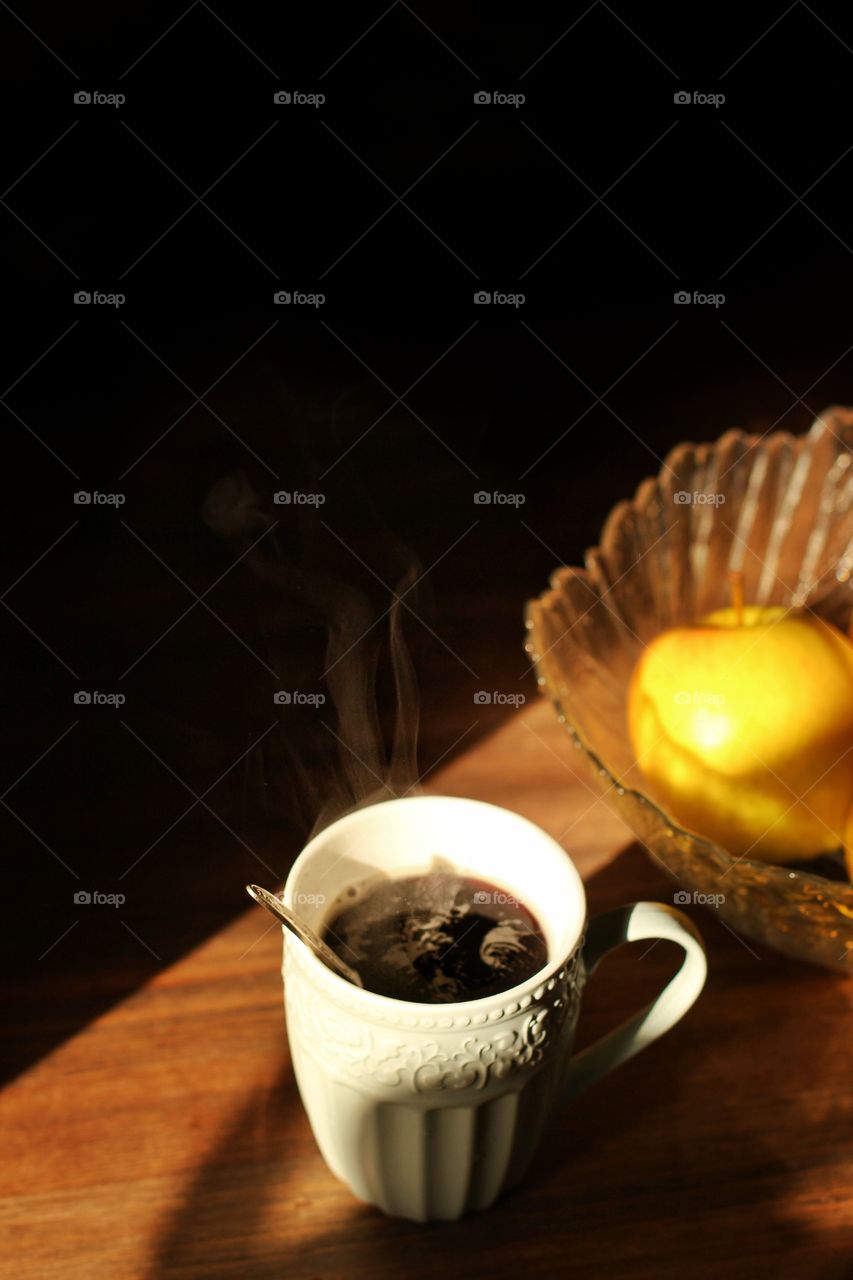 A cup of hot evening coffee and apples on a table in the kitchen