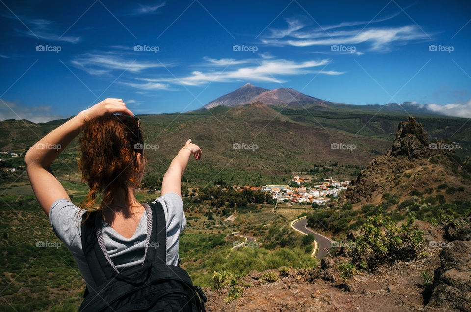 Young woman tourist with a backpack shows her hand on the the peak of the volcano Teide, Tenerife, Canary Islands, Spain