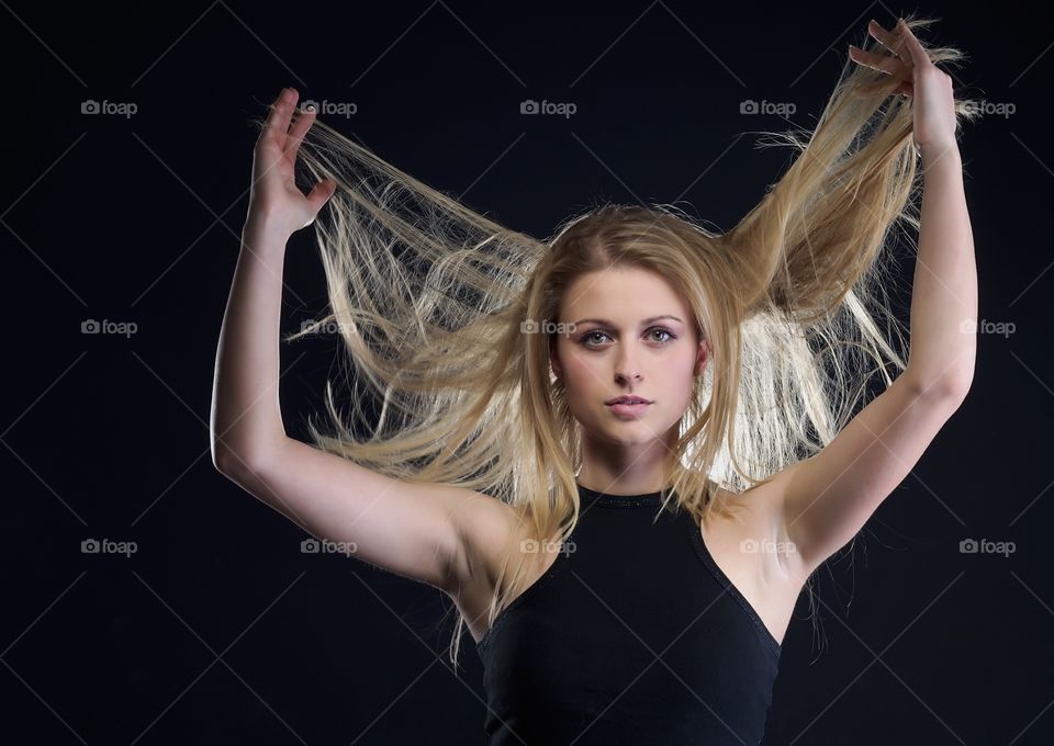 Young woman holding blonde hair against black background