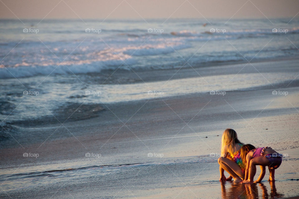 Two young children play in the sand at the ocean