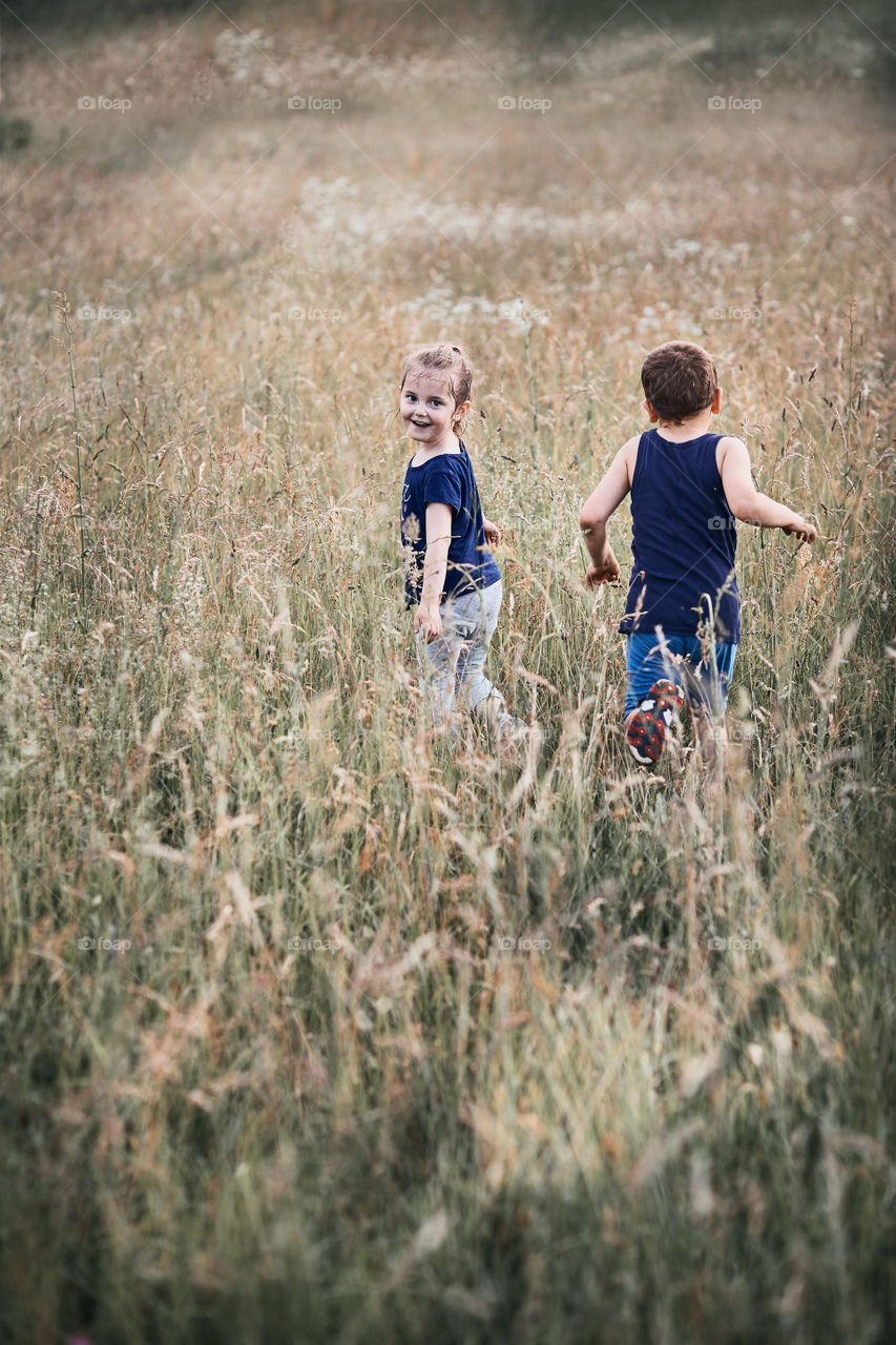 Little happy kids playing in a tall grass in the countryside. Candid people, real moments, authentic situations