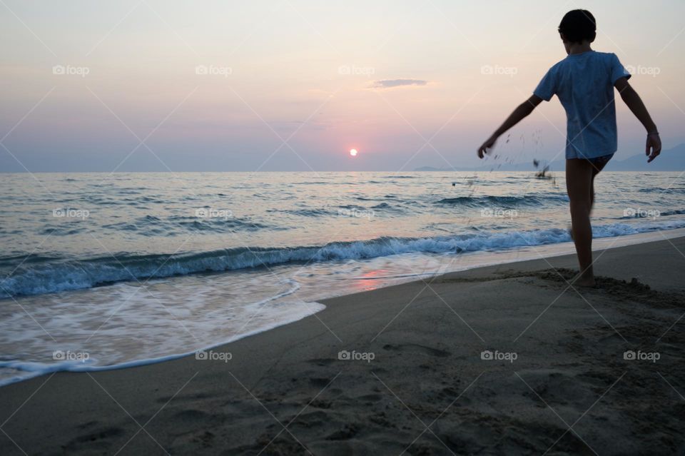 little boy kicking the sand at sunset in summer