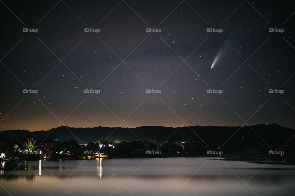 Comet Neowise passing over a lake in star filled sky