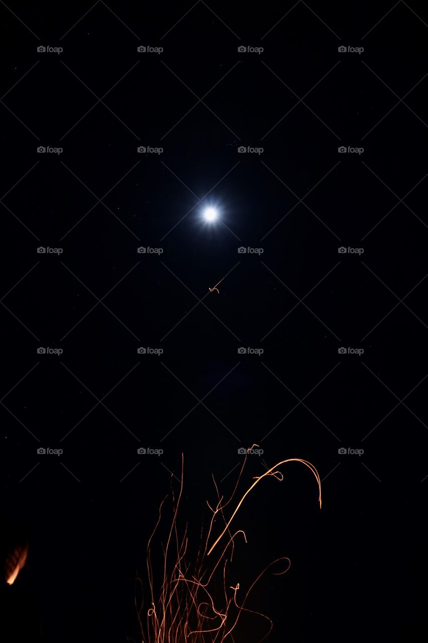 A calm night with a full moon and sparks from a fire.