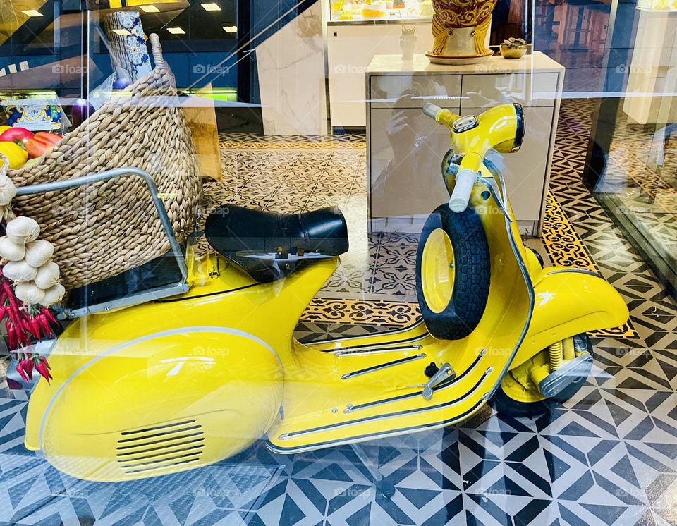 A yellow scooter sits prettily in a display window   