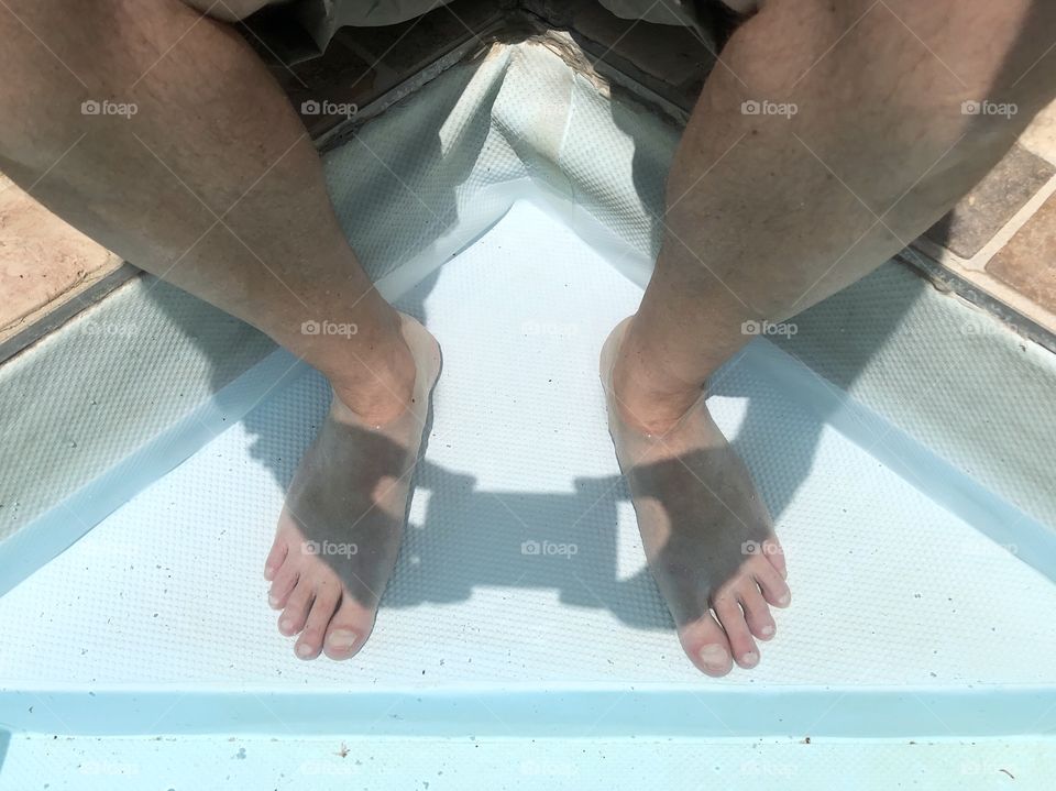 Sitting on pool edge with feet in water and shadow of hands with smartphone taking a picture