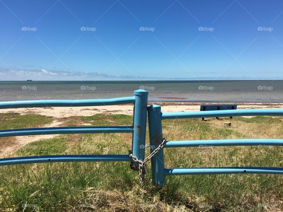 Incredible beach, view or beach and ocean horizon through weathered blue metal gate with chain and padlock 