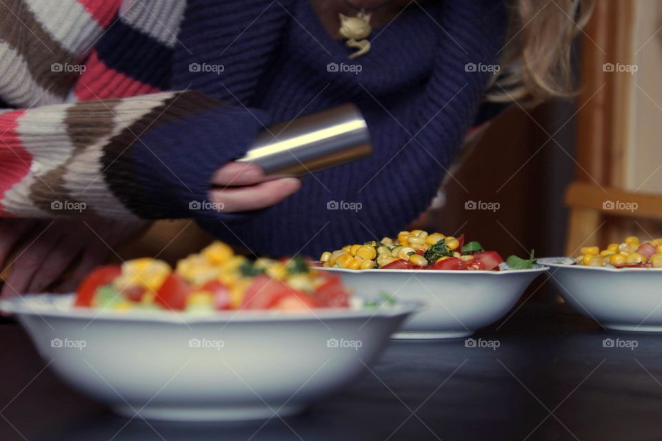 View of a table with a salad bowl and a woman holding a salt shaker