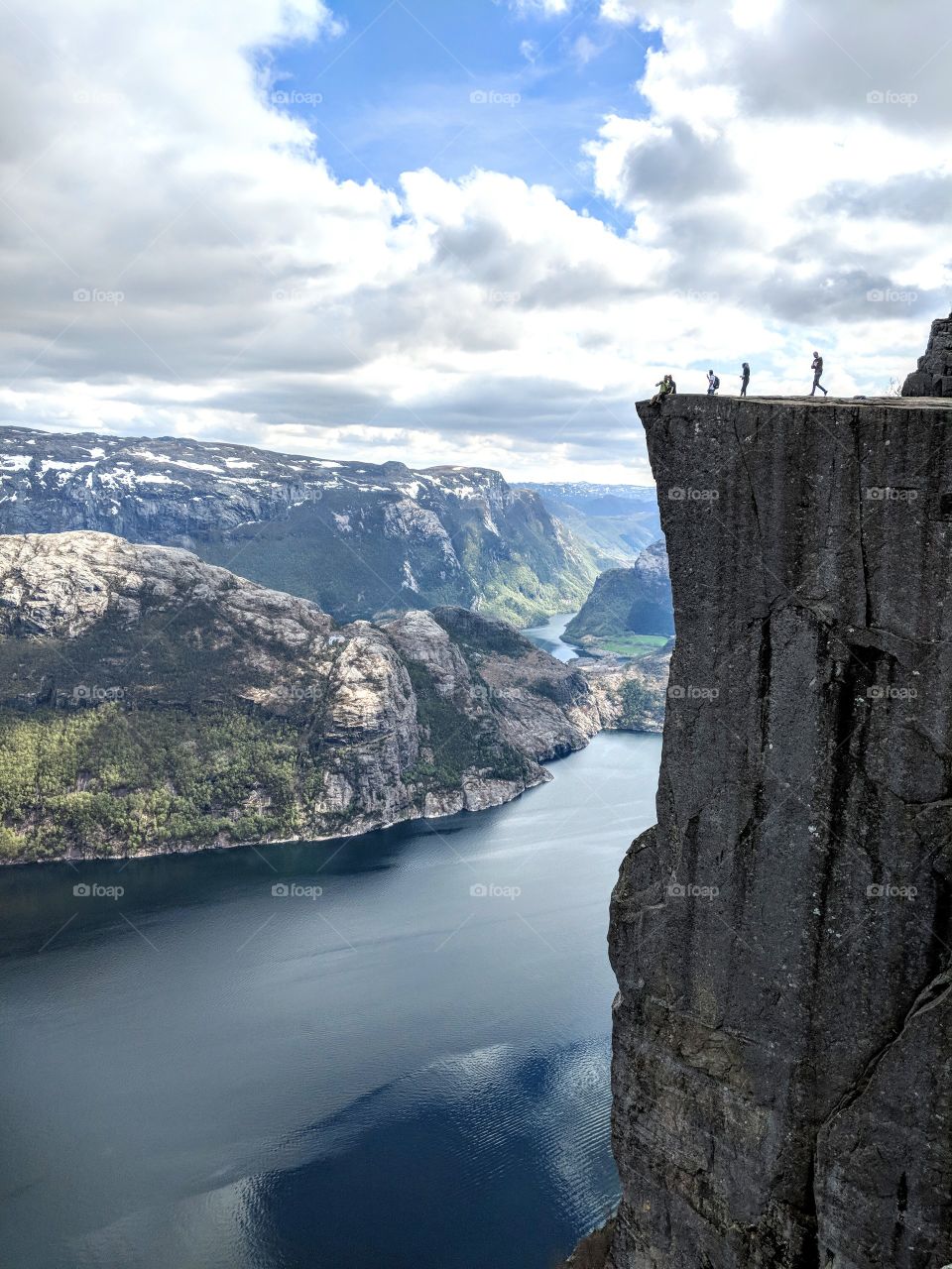 Beautiful fjord (mountain cliff by river) people moving to the edge on top and mountains and lakes in the background in Norway