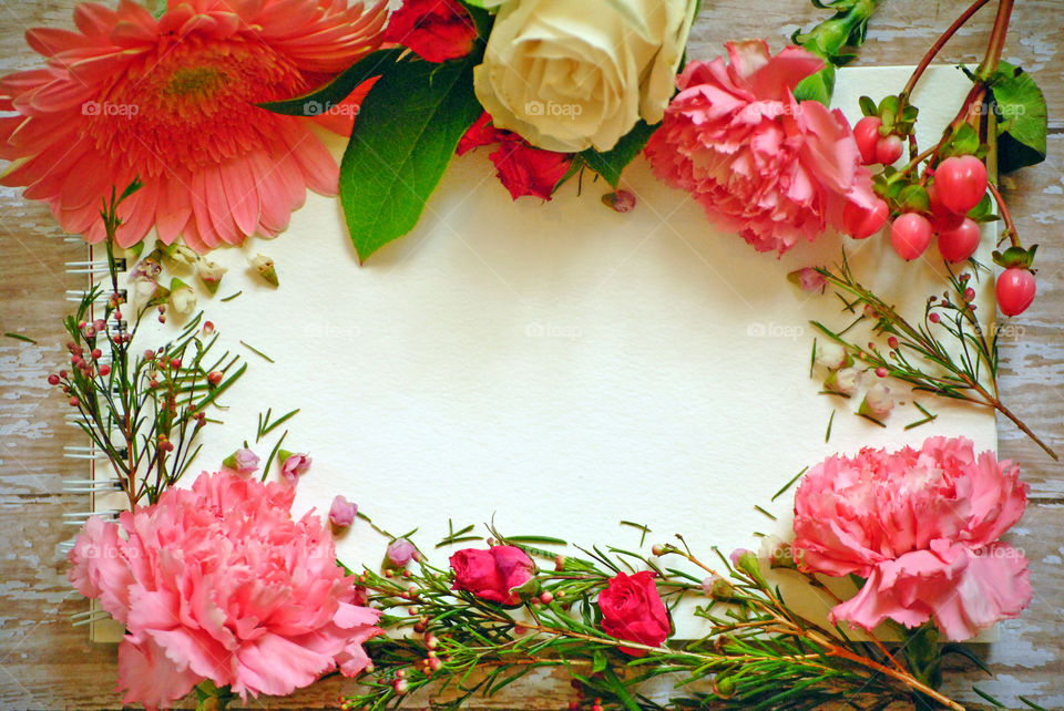 Spring, flowers, floral border, flower border, flat lay, white paper, wooden background, pink flowers and leaves, carnations, landscape orientation