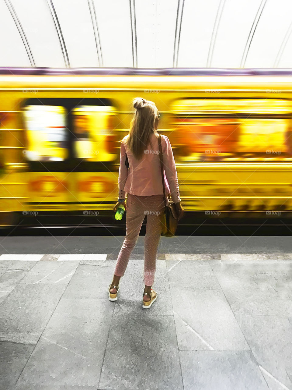 Young woman waiting for a subway train standing in front of a moving yellow train 