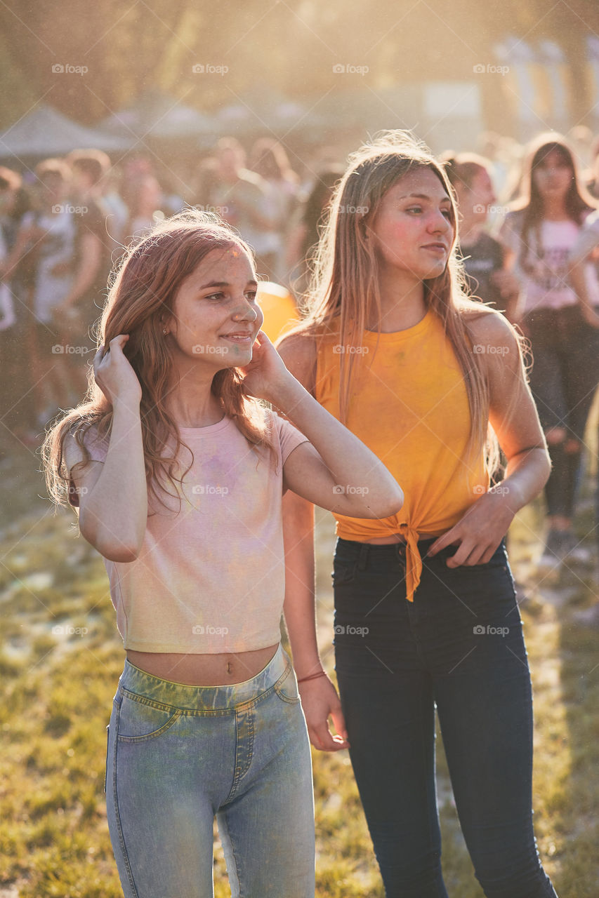 Portrait of happy smiling young girls with colorful paints on faces and clothes. Two friends spending time on holi color festival. Real people, authentic situations