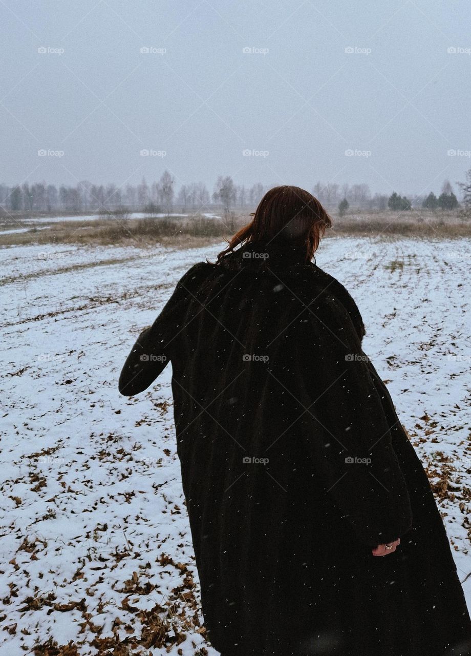 Freeze frame during a winter walk of a girl in a wild snowy field amidst falling snow