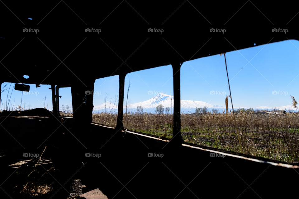 View from inside of an abandoned and rusty old Soviet Russian bus in the middle of reeds and agriculture fields with snow-capped scenic Ararat mountain and clear blue sky on the background in rural Southern Armenia in Ararat province on 4 April 2017.