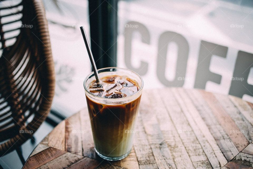 An iced latte was placed on a rustic wooden table in front of the cafe's window.