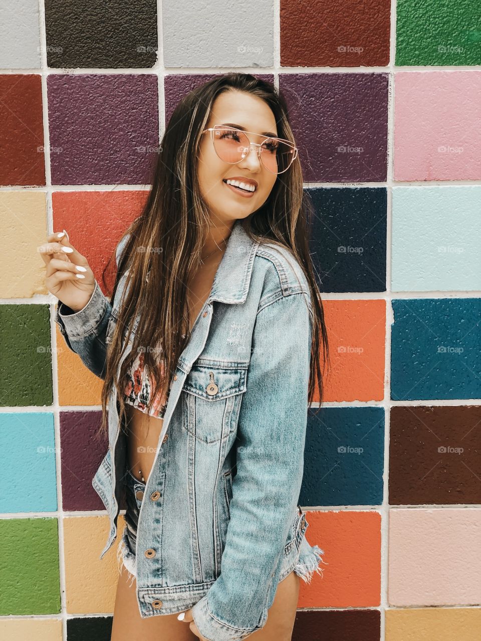 Pretty girl posing in front of a colorful art wall with her fun pink sunglasses.