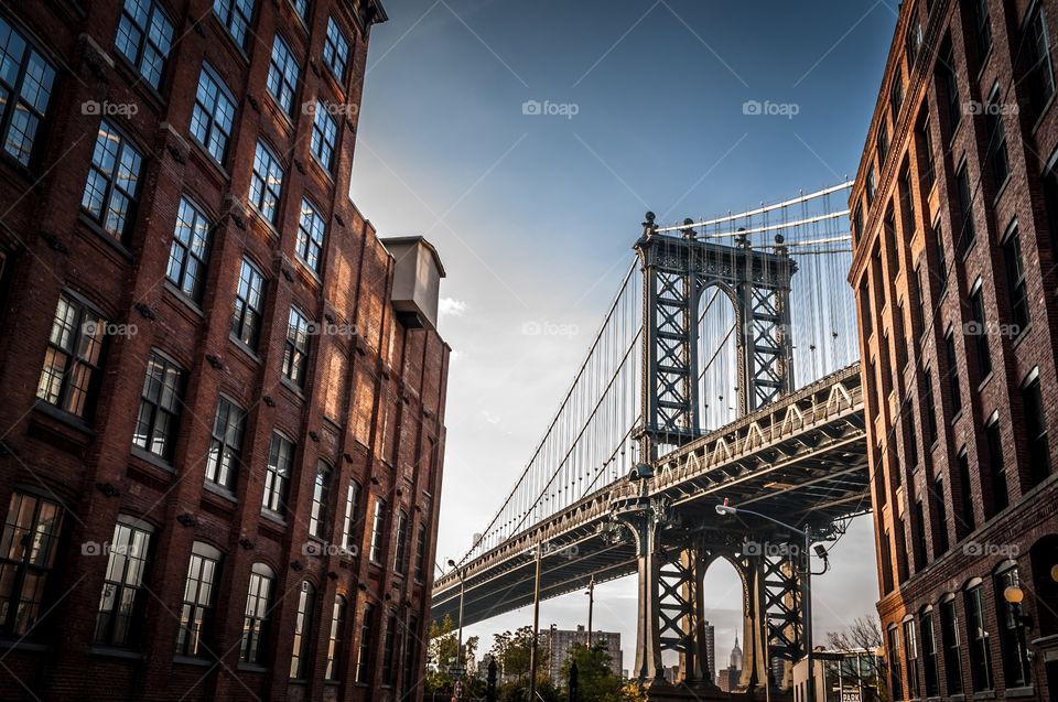 Manhattan bridge seen from  a narrow alley enclosed by two brick buildings on a sunny summer day 
