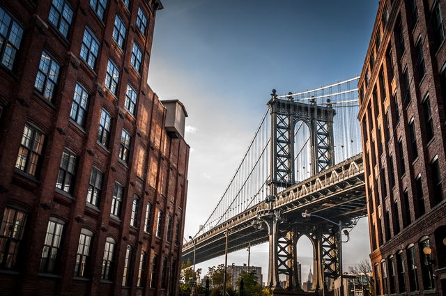 Manhattan bridge seen from  a narrow alley enclosed by two brick buildings on a sunny summer day 