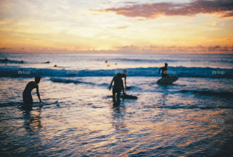 Surfers entering the water on the north shore of Oahu during sunset.